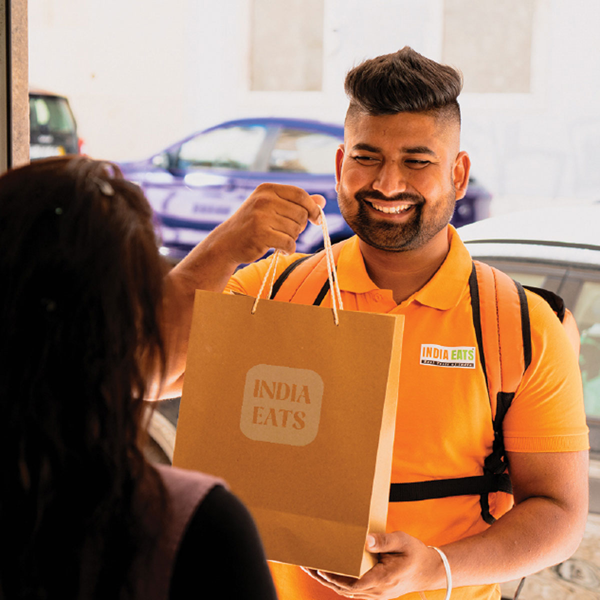 Entregador sorridente da India Eats entregando sacola para cliente